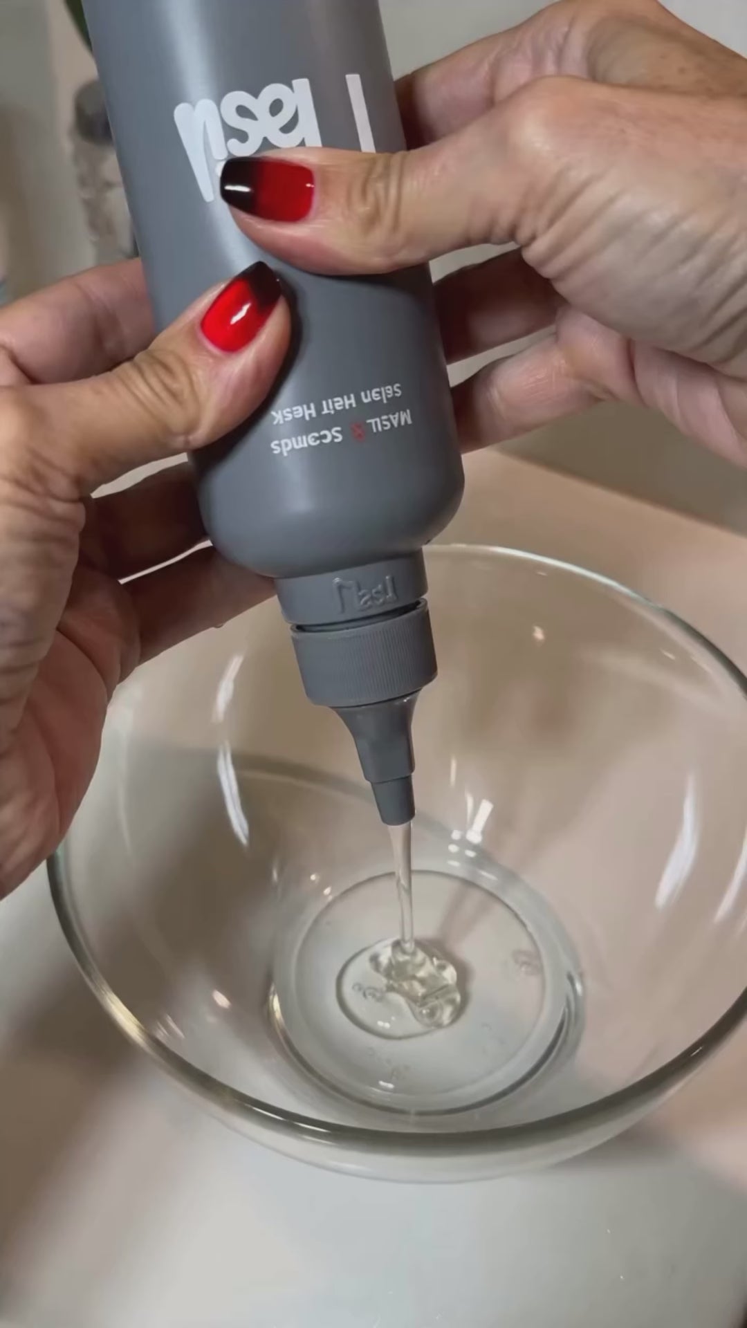 Video of MASIL 8 Seconds Salon Hair Mask showing the clear liquid formula transforming into a rich white cream, a woman applying the treatment to wet hair in the shower, and the final result of a smooth, glossy reddish-brown bob, followed by a close-up of the product bottle on a shower shelf.