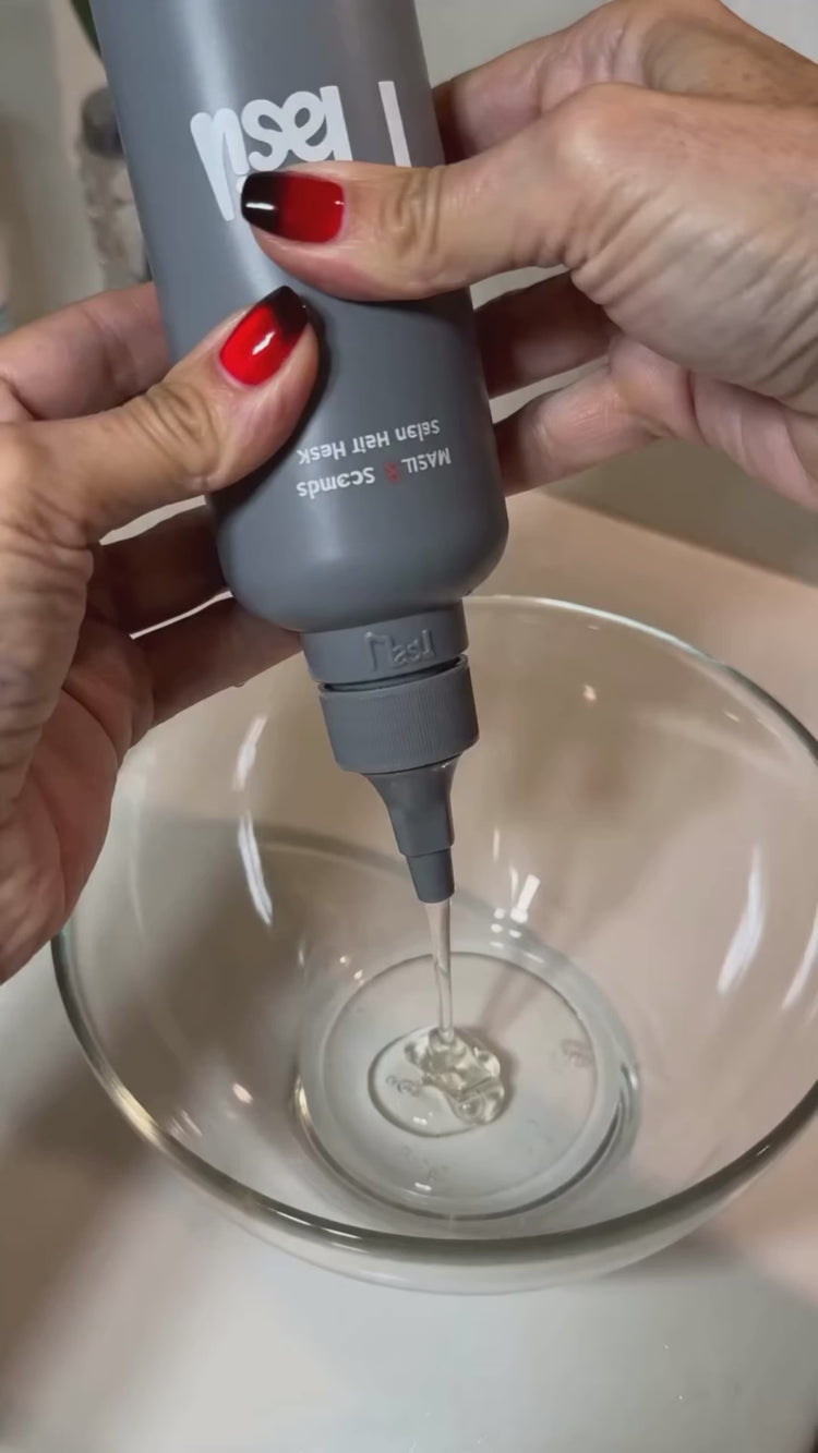 Video of MASIL 8 Seconds Salon Hair Mask showing the clear liquid formula transforming into a rich white cream, a woman applying the treatment to wet hair in the shower, and the final result of a smooth, glossy reddish-brown bob, followed by a close-up of the product bottle on a shower shelf.